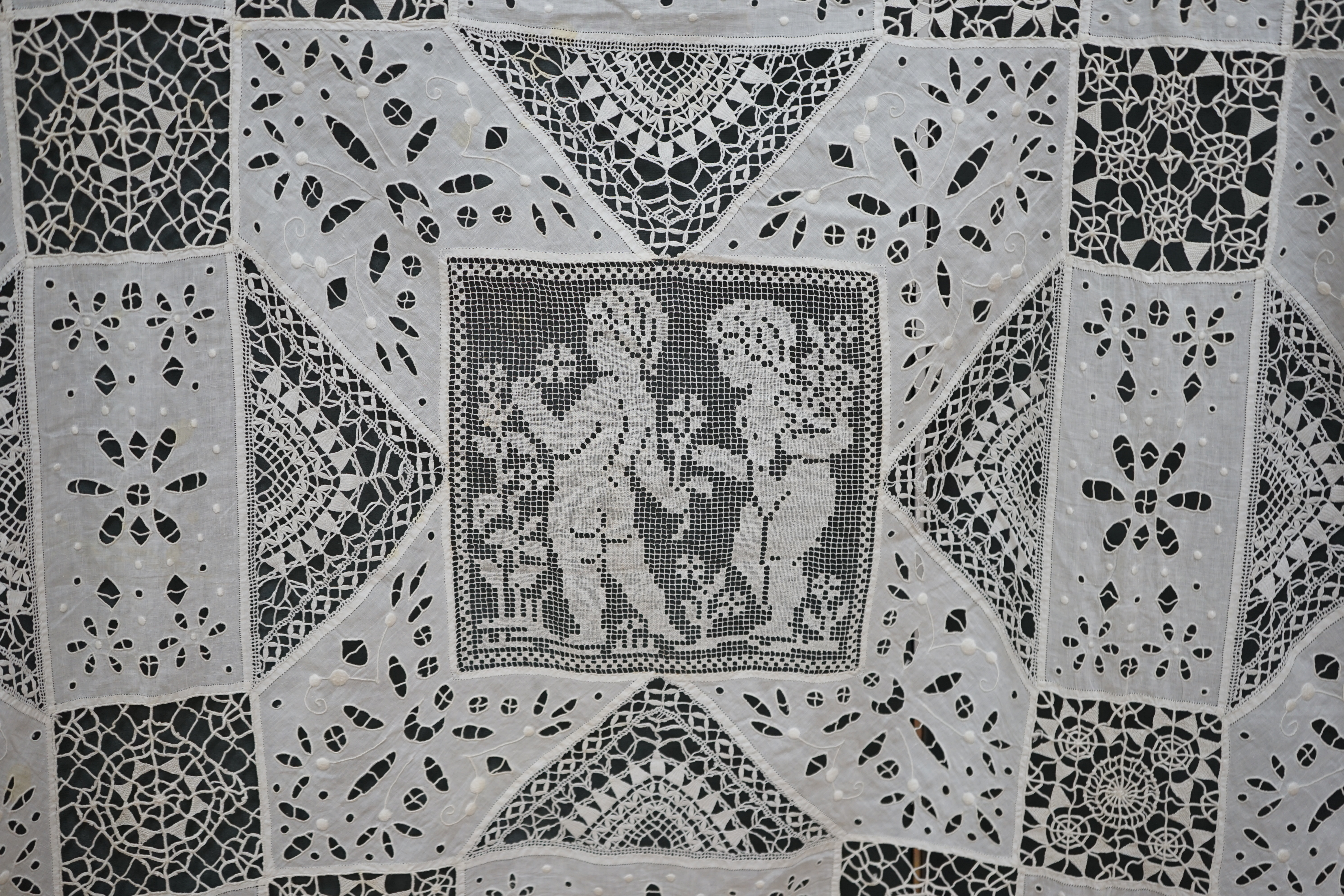 An early 20th century Italian ornate bedcover, worked with square fillet lace insertions of putti, white multi patterned cut work squares on fine linen and similar multi patterned needle lace squares, creating a unique b